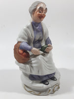 Old Woman Sitting with Basket of Bread Holding a Pear and Banana 6 1/2" Tall Porcelain Figurine